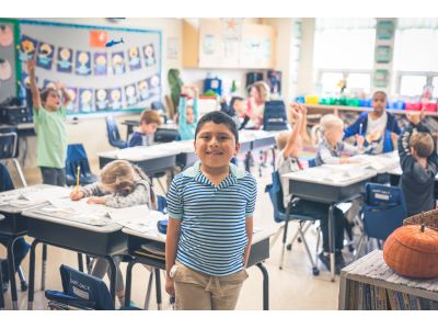 A student standing in a classroom, smiling at the camera.